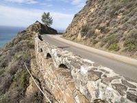 a large stone wall and a curved road by the ocean side in california, usa