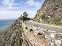 a large stone wall and a curved road by the ocean side in california, usa