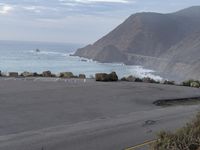 a man riding a skateboard on the side of a road by the ocean along a cliff