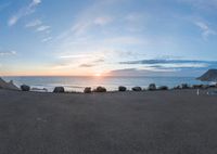 view of a sandy beach and ocean during sunset with a bench sitting in the middle