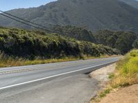 a small stop sign is near an empty road near a mountain peak and hillside in california