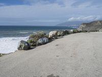 a bunch of rocks by the ocean on a road in front of a cliff with waves