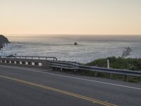 a curve road that is near the beach near the ocean at sunset or sunrise hours