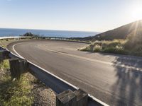 a curved curve road leading to the ocean with an ocean view in the background and a large sign at the corner reading turn of the left