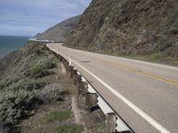 a motorcycle travels down the highway beside a cliff near the ocean and a cliff with a road side