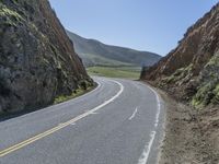 the road has two yellow lines in the middle of it and on the side is an open cliff