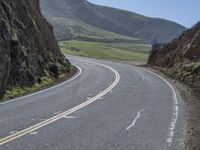 the road has two yellow lines in the middle of it and on the side is an open cliff