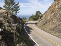 a lone motorcycle is riding down the winding road on the ocean cliffs side near an island