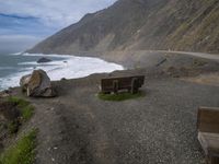 a wooden bench sits on the shoreline of a beach near the ocean with mountains behind it