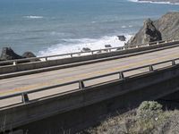 a road going over an old bridge near the ocean, with a view to the sea