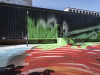 a bike on a rainbow painted road by a building with stairs in the background and a painting of green leaves