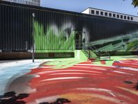 a bike on a rainbow painted road by a building with stairs in the background and a painting of green leaves