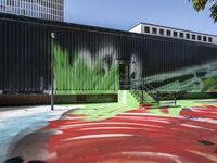 a bike on a rainbow painted road by a building with stairs in the background and a painting of green leaves