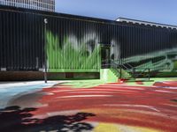 a bike on a rainbow painted road by a building with stairs in the background and a painting of green leaves