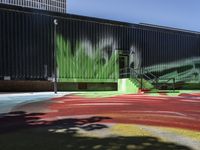 a bike on a rainbow painted road by a building with stairs in the background and a painting of green leaves