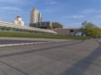 a woman riding on the side of a road next to a park with buildings in the background