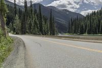 a bike rider riding up the side of a road past trees on it with mountains in the distance