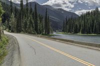 a bike rider riding up the side of a road past trees on it with mountains in the distance