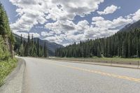 a bike rider riding up the side of a road past trees on it with mountains in the distance