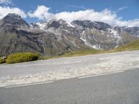 a picture of a bike rider on a mountainous road with snow capped mountains in the background