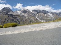 a picture of a bike rider on a mountainous road with snow capped mountains in the background