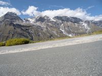 a picture of a bike rider on a mountainous road with snow capped mountains in the background