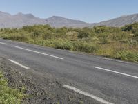 a person is riding a bike down the side of the road near some mountains and bushes