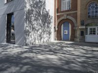 a man on a bike riding down a sidewalk near some buildings and a tree with a blue door