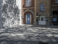 a man on a bike riding down a sidewalk near some buildings and a tree with a blue door