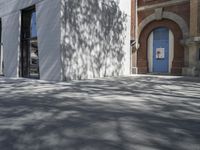 a man on a bike riding down a sidewalk near some buildings and a tree with a blue door