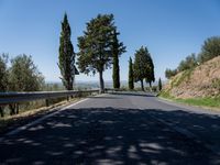 a couple of bikers are riding down the road near some trees and bushes and hills