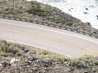 a person is riding a bike on the road next to the ocean with a surfboard