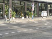 a person riding on the street by a bike outside of a storefront window in front of a street sign with trees