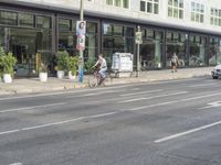 a person riding on the street by a bike outside of a storefront window in front of a street sign with trees