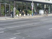 a person riding on the street by a bike outside of a storefront window in front of a street sign with trees