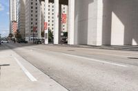 the man is riding his bike down the city street with pedestrians nearby and other cars in front