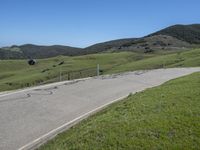 a person on a bike on a mountain road with hills in the background, with an empty roadway next to it