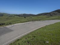 a person on a bike on a mountain road with hills in the background, with an empty roadway next to it