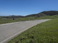 a person on a bike on a mountain road with hills in the background, with an empty roadway next to it