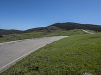 a person on a bike on a mountain road with hills in the background, with an empty roadway next to it