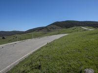 a person on a bike on a mountain road with hills in the background, with an empty roadway next to it