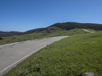 a person on a bike on a mountain road with hills in the background, with an empty roadway next to it