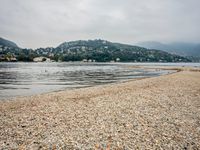 birds walking on the shore line of a calm beach with mountains in the background, during an overcast, dark, cloudy day