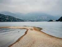 birds walking on the shore line of a calm beach with mountains in the background, during an overcast, dark, cloudy day