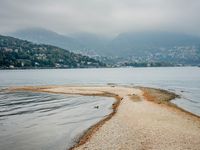 birds walking on the shore line of a calm beach with mountains in the background, during an overcast, dark, cloudy day