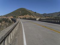 a freeway bridge with a curve around the road and mountains in the background with a yellow painted line in the foreground