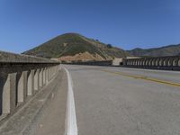 a freeway bridge with a curve around the road and mountains in the background with a yellow painted line in the foreground