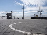 a circle has been drawn in the street by a dock with water behind it and birds flying overhead