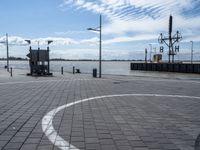 a circle has been drawn in the street by a dock with water behind it and birds flying overhead