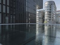 black building reflecting off the water on the edge of a city canal with a man and woman